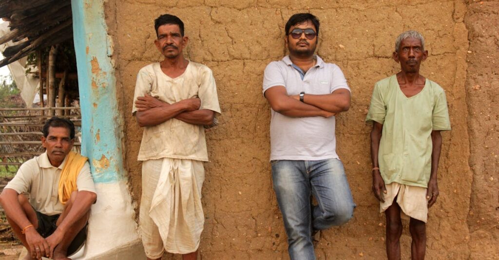 Four men standing and sitting against a mud wall in Balaghat, India.