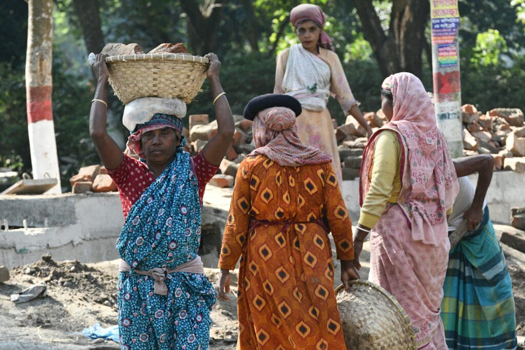 South Asian women laborers working outdoors in Rangpur, Bangladesh, carrying baskets and bricks.